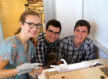 Rice University students -- from left, Liz Kacpura, Noah Kenner and Caz Smith – demonstrate their Ro Sham Bot, a rock-paper-scissors robot, at an exhibition by engineering students of mechatronic art at Rice's Moody Center for the Arts. (Credit: Donald Soward/Rice University)