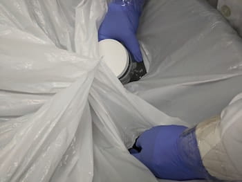 Rice University research scientist Varun Shenoy Gangoli puts gloved hands and a container into holes in a bag set up to contain nanomaterials while transferring them from bulk containers into smaller ones for lab use. The technique helps the lab keep nanomaterials from escaping into the environment. (Credit: Barron Research Group/Rice University)