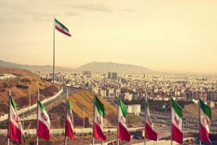 A row of Iranian flags against the backdrop of the Tehran skyline
