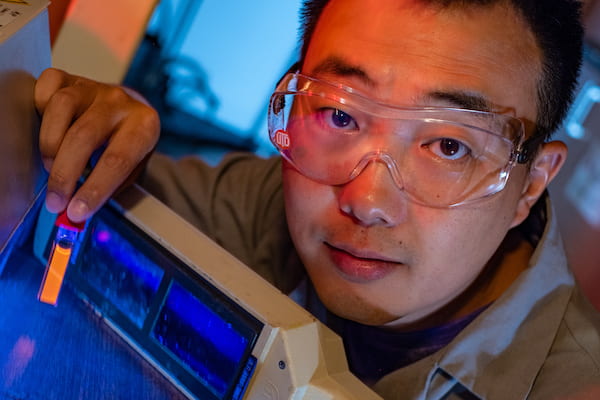 Rice University graduate student Bo Jiang shows a fluorescing vial of soluble amyloid beta peptide aggregates implicated in the onset of Alzheimer's disease. The peptides are tagged and tracked with a ruthenium complex developed at Rice that can monitor them in lab experiments as they grow over time. (Credit: Jeff Fitlow/Rice University)