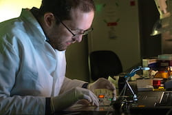 Rice University graduate student Thomas Heiderscheit demonstrates a technique to amplify the light from small concentrations of molecules on a surface by maximizing the spectral overlap between the emission and the plasmon resonance of adjacent nanoparticles. The glowing molecules can be clearly seen in the sample when excited. (Credit: Jeff Fitlow/Rice University)