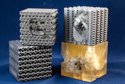 Tubulane-like polymer structures created at Rice University were better able to handle the impact of a bullet than the polymer reference cube at bottom right. The bullet stopped in approximately the second layer of the tubulane structures, with no significant structural damage observed beyond that layer. Bullets fired at the same speed sent cracks through the entire reference cube. (Credit: Jeff Fitlow/Rice University) 
