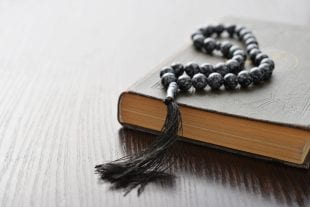 Holy Quran with beads over wooden background closeup.